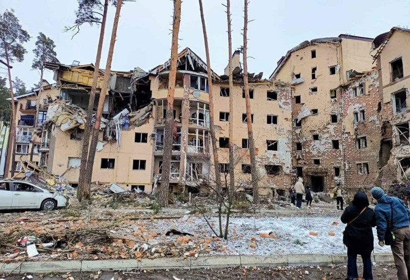 Wenige Menschen, die vor einem zerstörten Haus mit vielen Stockwerken stehen.