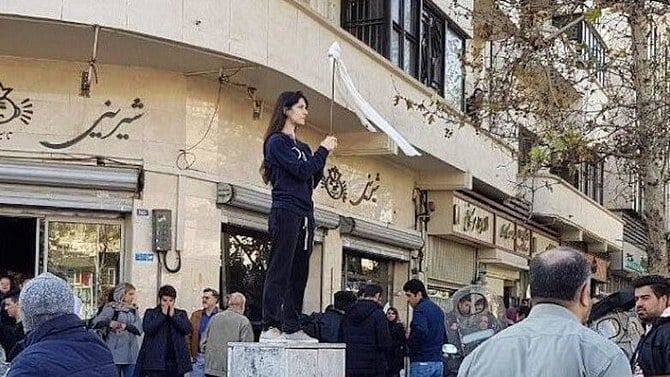 Eine Frau in schwarzer Kleidung mit einer weißen Fahne in einer Protestszene.