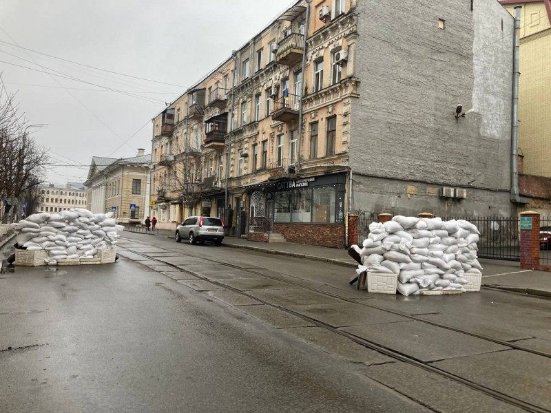 Several white sacks stacked on a street with residential buildings.