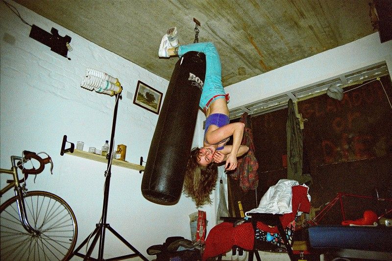 Eine Frau hängt kopfüber an einem Boxsack und lacht.