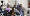 Group of people sitting along a U-shaped table and discussing with a standing person who is smiling.