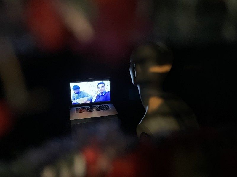 Eine Figur die auf einen Laptop guckt, auf dem sie eine Videokonferenz mit zwei Personen hat.