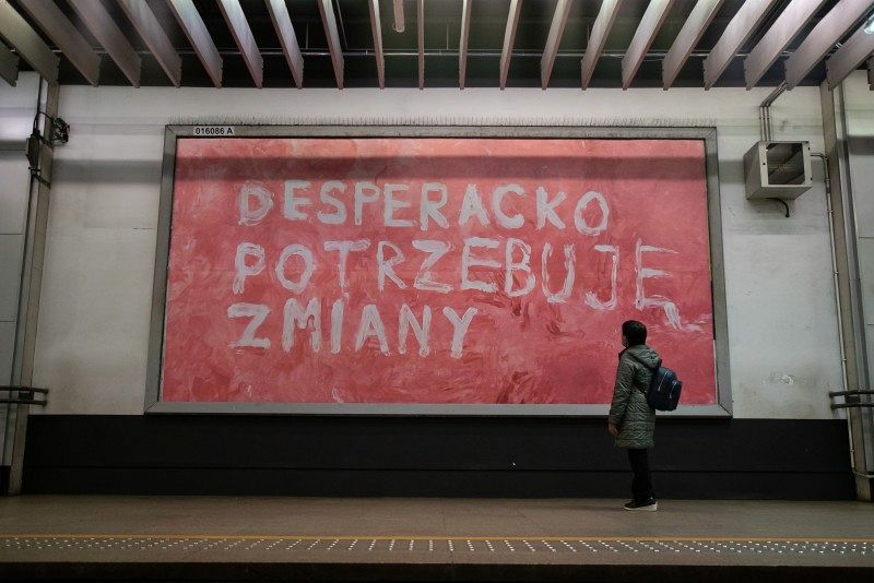 A person in front of a red screen with white writing in a subway station.