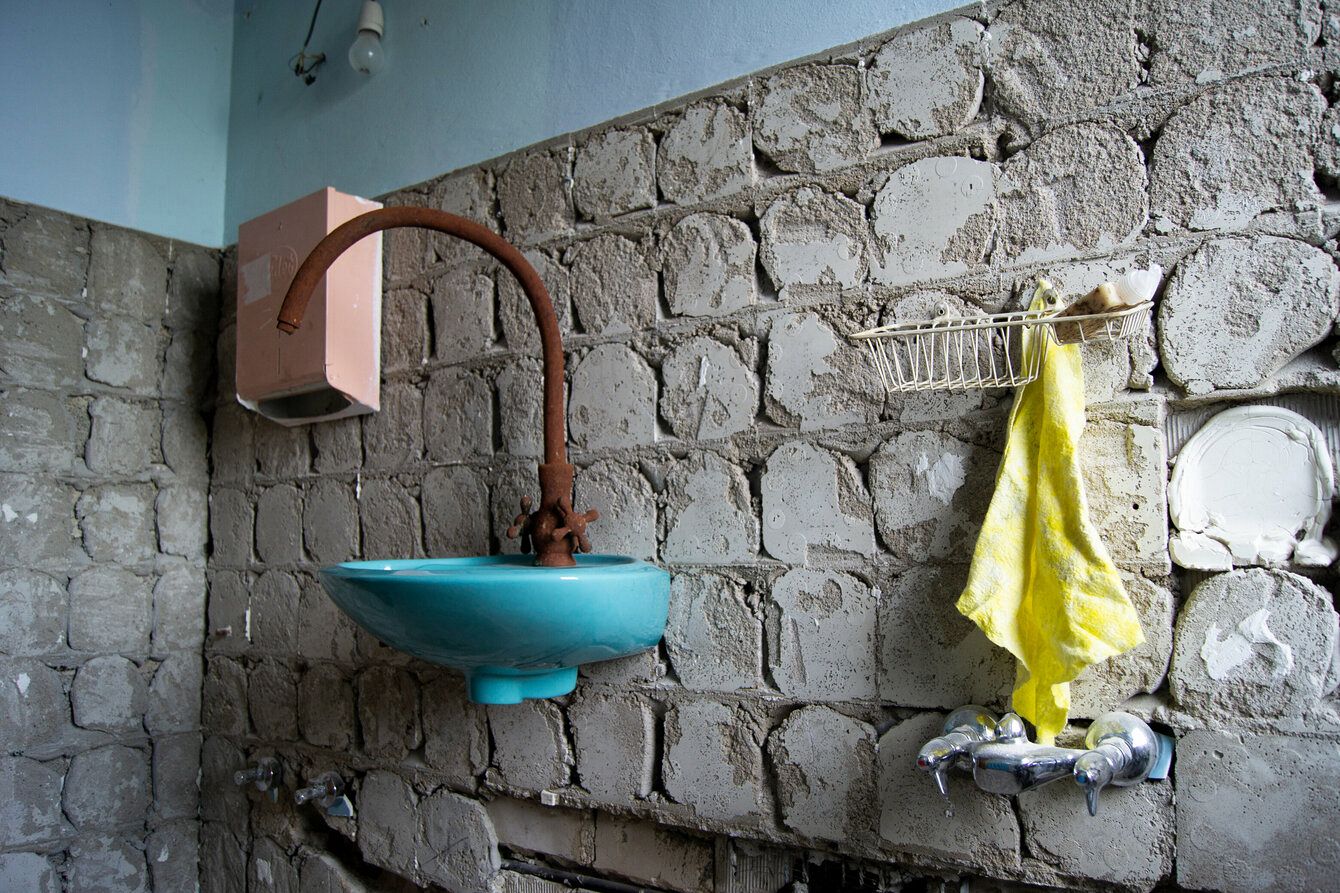 A turquoise-coloured washbasin hangs on a stone wall, with a yellow towel next to it.