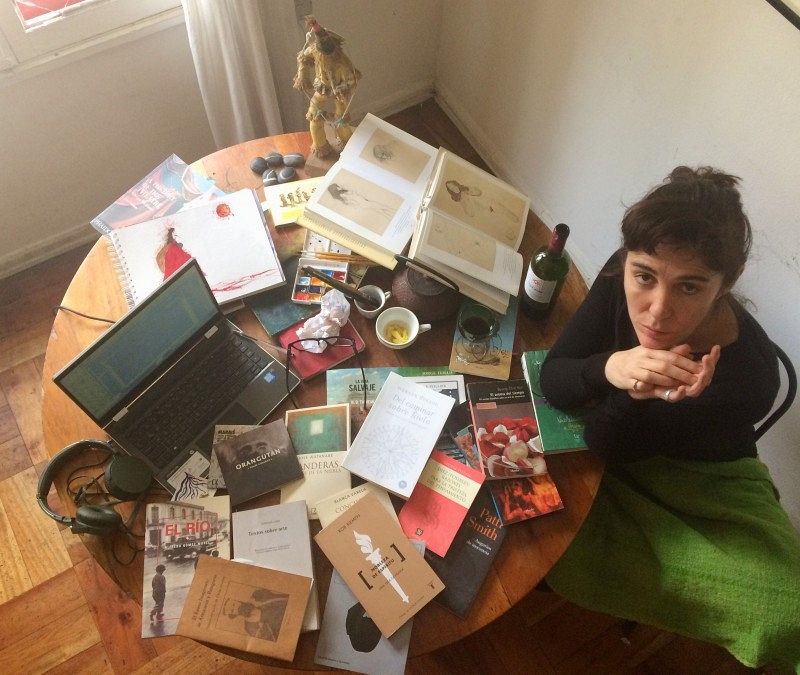 A woman at a table overflowing with books, a laptop and small items.